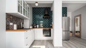A modern kitchen with white cabinets, a black range hood, and a stainless steel refrigerator. - Apartamenty Sun & Snow Róża Wiatrów (Gizycko)