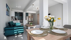 A modern living room with a teal sofa, a dining table set with plates and glasses, and a vase with flowers. - Apartamenty Sun & Snow Róża Wiatrów (Gizycko)
