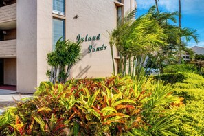 A building with a sign reading "Island Sands" surrounded by lush tropical plants. - Beautiful Oceanfront Condo, Huge Views near Harbor, AC! (Wailuku)