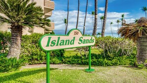 En skylt med texten ”Island Sands” och siffran ”150” ovanför, placerad mot en bakgrund av palmer och en byggnad.