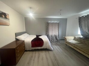 Un dormitorio con cama, cómoda, sofá y ventana con cortinas.