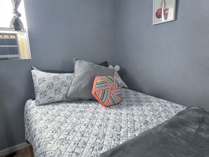 A bed with a patterned quilt, two pillows, and a striped pillow.