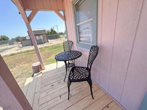 A covered outdoor area with a wooden deck, two metal chairs, and a table.