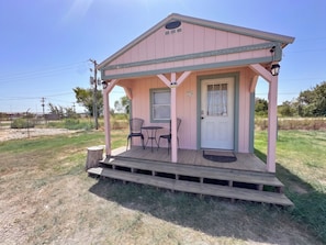 A pink building with a porch, two chairs, and a table. - TH Monthly + Utilities + Laundry + Comfy Stay! (Grant)