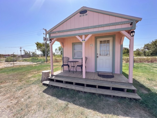 A pink building with a porch, two chairs, and a table.
