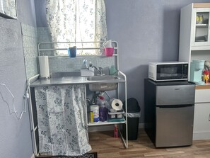 A compact kitchen with a microwave, a refrigerator, a sink, and a small shelf with various items.