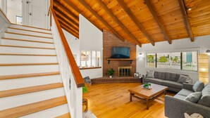 A spacious living room with a wooden staircase, a fireplace, a large window, and a comfortable seating area. - Perfect For Families, Walk To Beach, Rooftop Deck* (Oxnard)