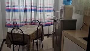 Una pequeña cocina con una mesa de comedor, sillas, un dispensador de agua y un refrigerador.