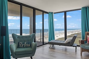 Un balcon avec vue sur la plage, une chaise longue, un fauteuil rembourré avec un coussin et une chaise en osier.