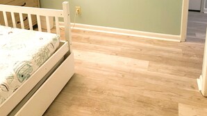 A room with a wooden floor, a white crib, a dresser with drawers, and a wall socket. - Bright & Spacious Direct Oceanfront 3BR Condo in North Myrtle Beach! (North Myrtle Beach)