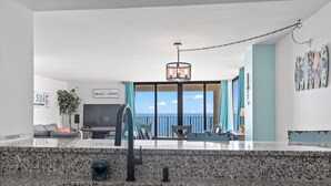 A modern kitchen with a granite countertop, a stainless steel sink, and a dining area with a view of the ocean. - Bright & Spacious Direct Oceanfront 3BR Condo in North Myrtle Beach! (North Myrtle Beach)
