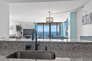A modern kitchen with a granite countertop, a stainless steel sink, and a dining area with a view of the ocean.