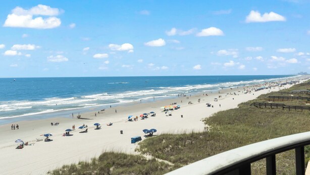 A beach with umbrellas and people, a clear sky, and the ocean. - Bright & Spacious Direct Oceanfront 3BR Condo in North Myrtle Beach! (North Myrtle Beach)