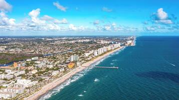 Vista aérea de una ciudad costera con una extensa playa, una zona urbana densa y un muelle que se adentra en el océano.