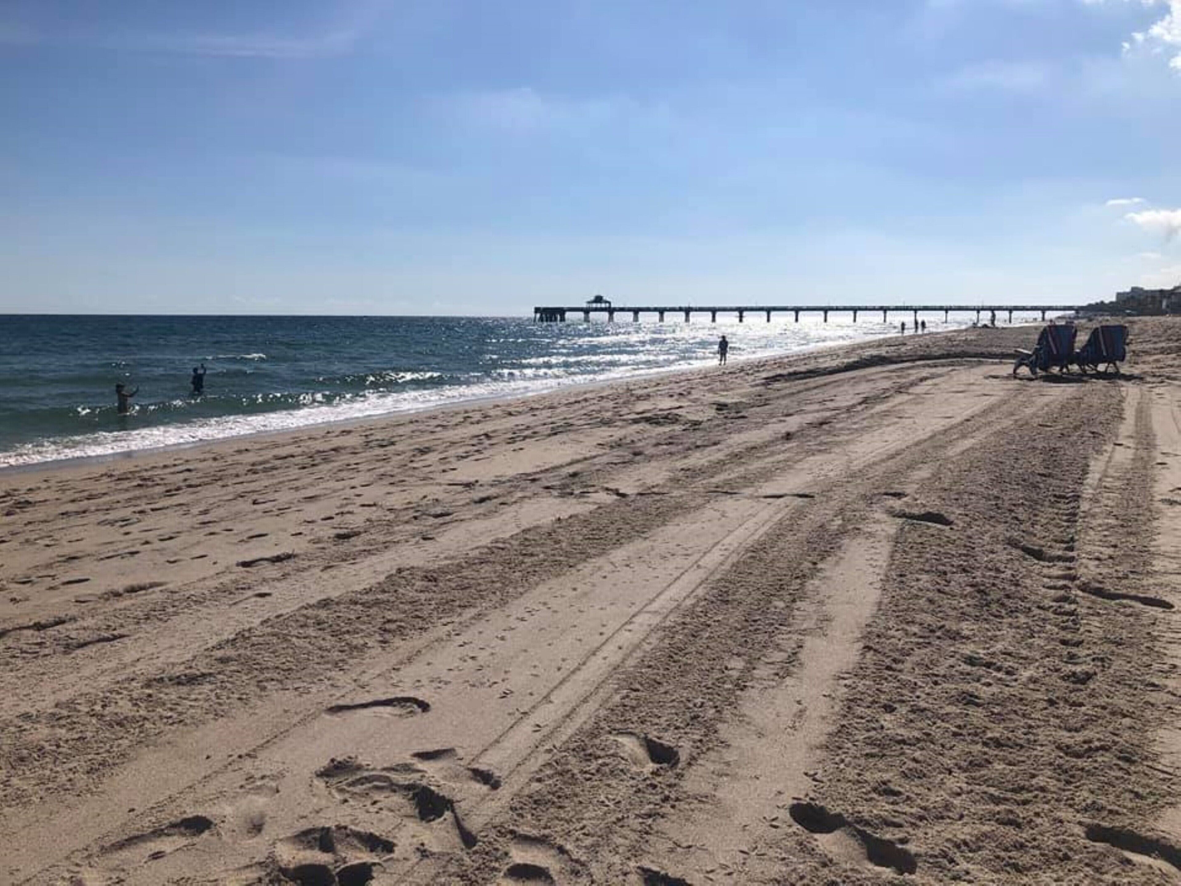 A beach with a pier extending into the water, sandy terrain, and footprints.