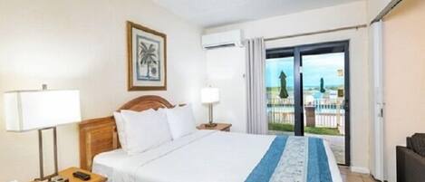 A hotel room with a bed, bedside tables, a lamp, a picture on the wall, and a sliding glass door leading to an outdoor area.