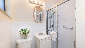 A bathroom with a toilet, sink, mirror, and shower.