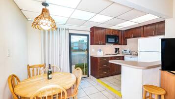 Cocina compacta con armarios de madera, microondas, refrigerador y comedor con mesa y sillas de madera.