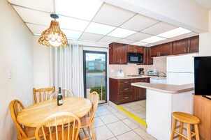 Cocina compacta con armarios de madera, microondas, refrigerador y comedor con mesa y sillas de madera.