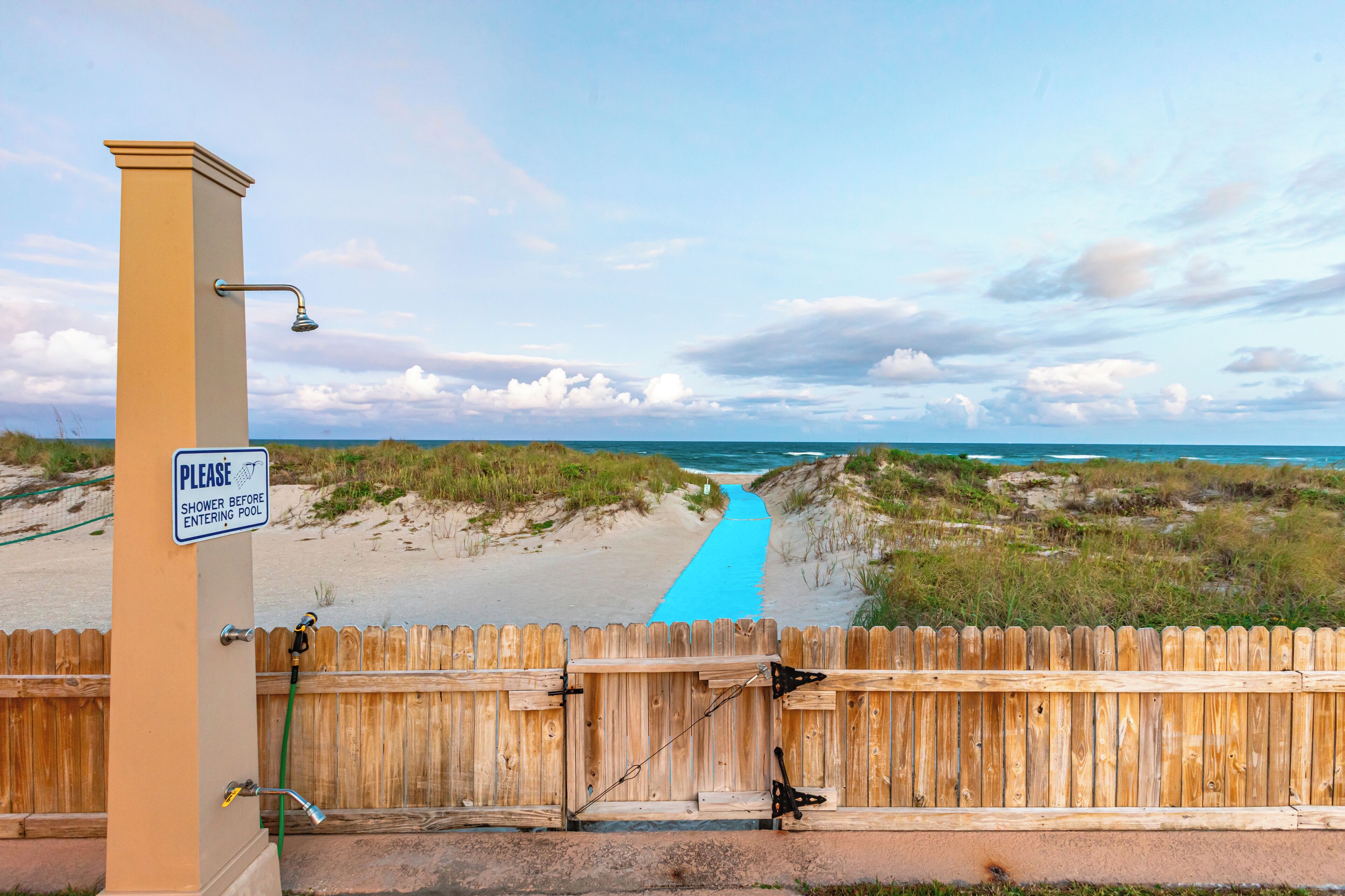 A wooden fence with a sign instructing to shower before entering the pool.