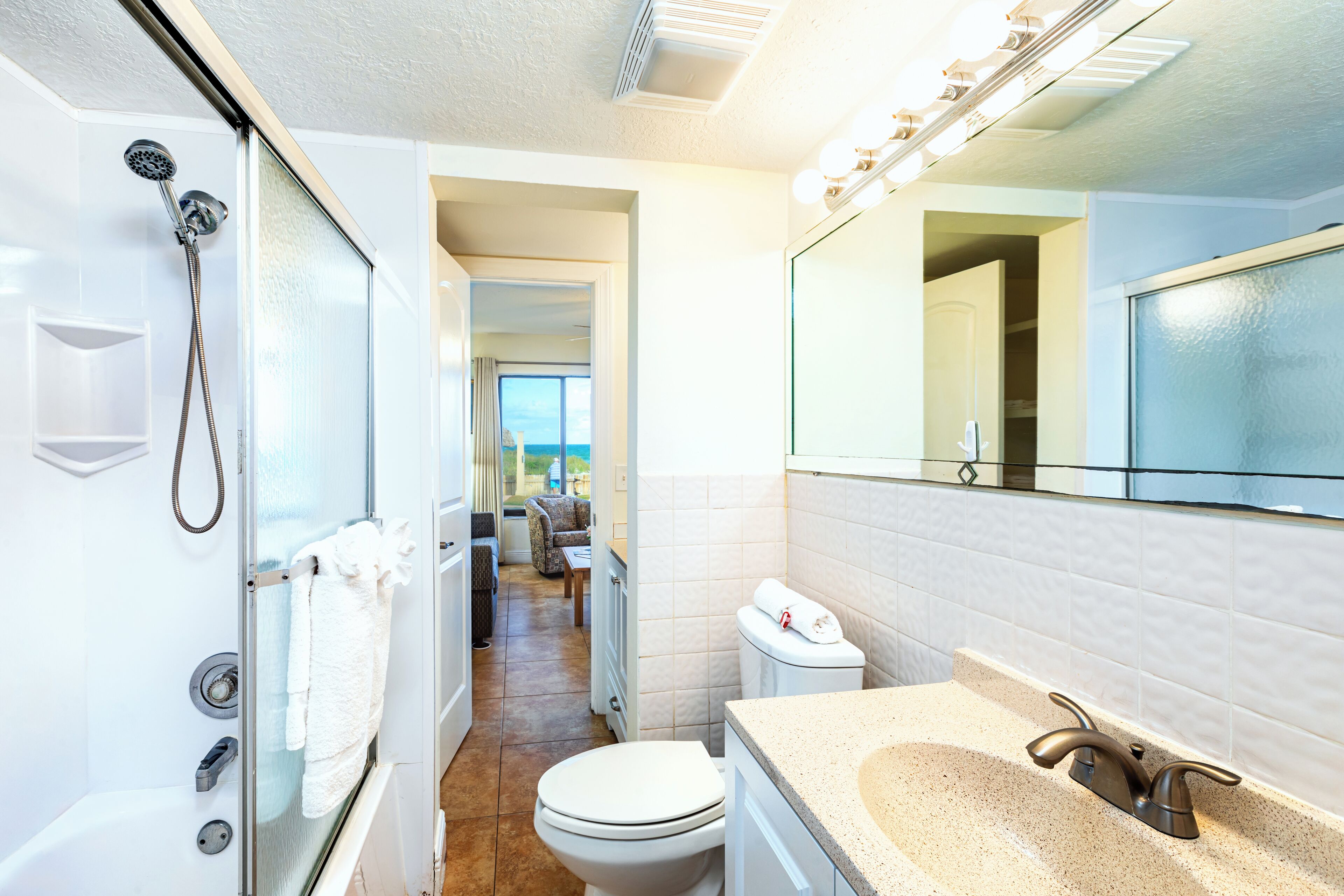 Un baño moderno con ducha envuelta en vidrio, inodoro blanco y encimera color beige con lavamanos.