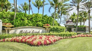 A landscaped area with a sign reading "Aldo's Creek," surrounded by lush greenery and palm trees. - Whisper Trace at Fiddlers Creek - 2 Bedroom Coach Home. (Naples)