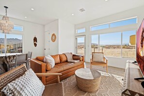Un salón amplio con un sofá de cuero, una zona de comedor con mesa de cristal y ventanas grandes con vistas al desierto.