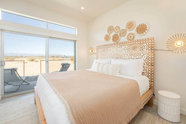 A bedroom with a large bed, a view through a sliding door, decorative wall art, and a small bedside table.