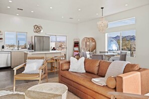 A spacious living area with a leather sofa, wicker chairs, and a view of a mountainous landscape through large windows.