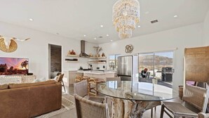 A modern kitchen with a central island, a dining area with a glass table, and a living room with a large TV.