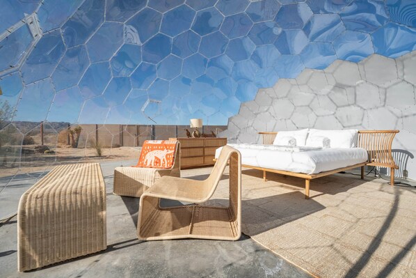 A room with a bed, a chair, a small table, and a view of the desert.