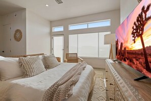 A bedroom with a bed, a television, a chair, and a large window.