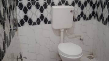 A bathroom with a toilet, a shower, and a tiled wall with a black and white pattern.