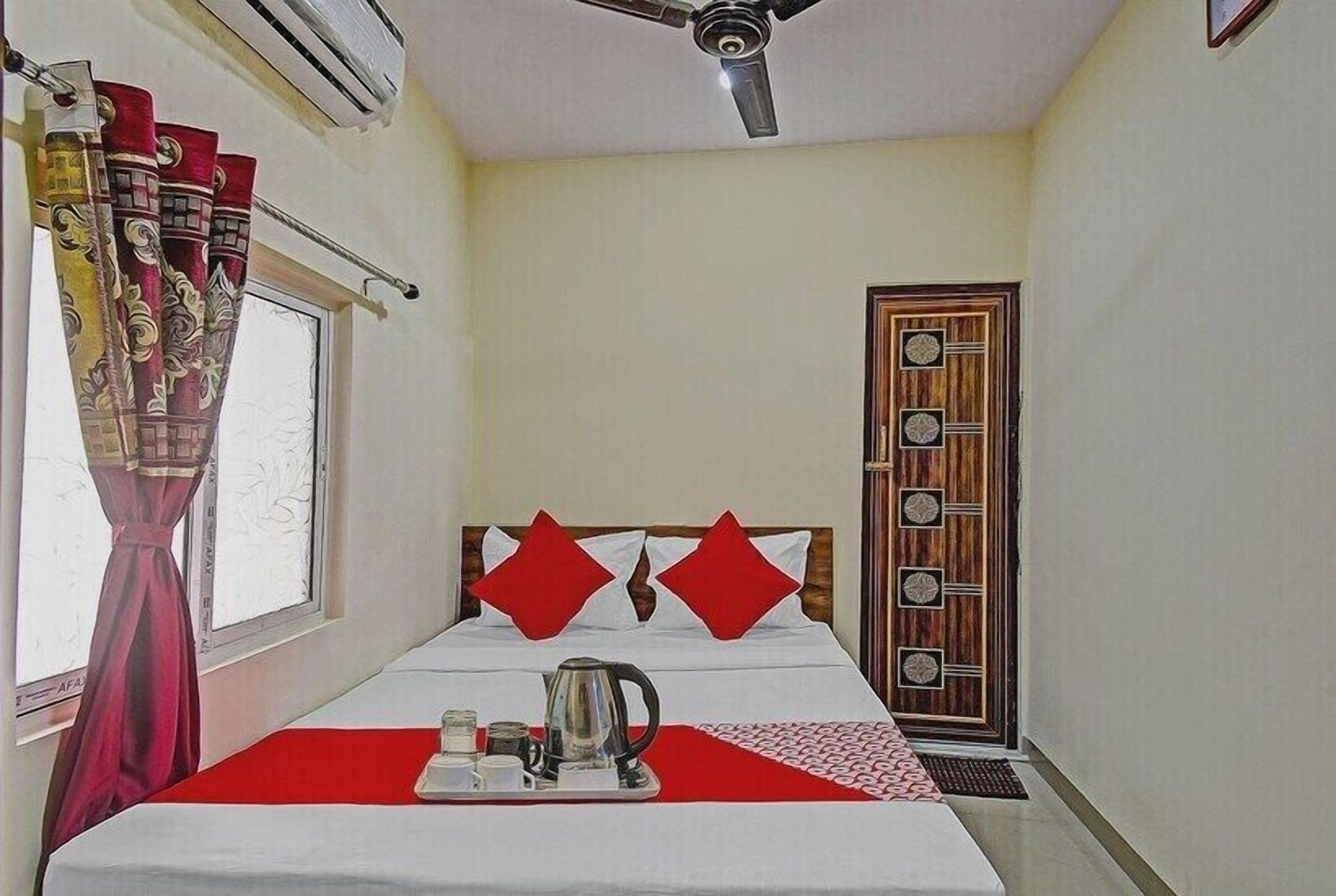Una habitación de hotel con cama, ventilador de techo, ventana con cortinas y puerta con panel decorativo.