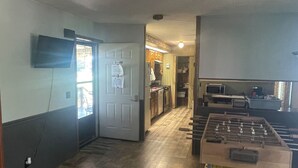 Una habitación con una mesa de fútbol, una puerta con un letrero y una cocina al fondo.
