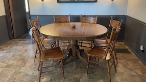 Una mesa de comedor redonda de madera con seis sillas, un cartel enmarcado que dice "FOUR ROSES RANCH EST 2024" y luces fijadas a la pared.