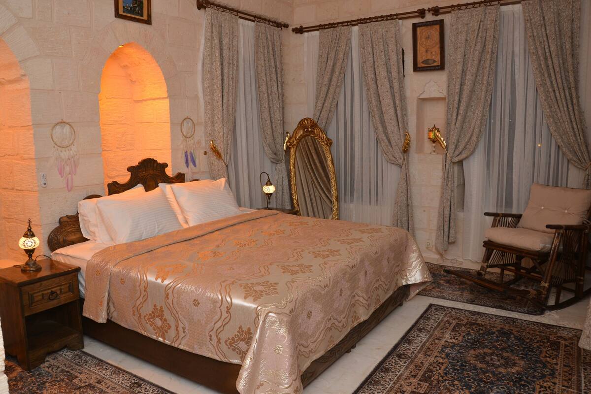 Un dormitorio con una cama grande, una mesita de noche, una silla y un espejo decorativo.