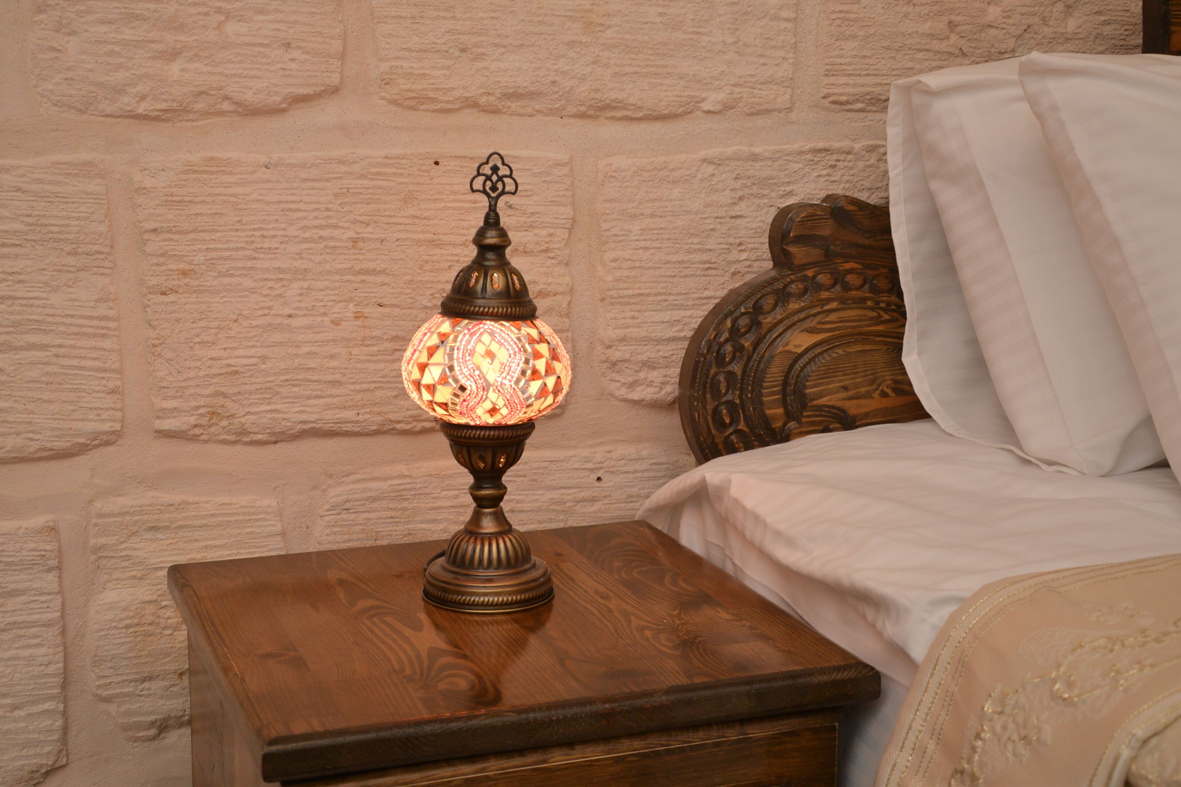 A wooden bedside table with a decorative lamp against a textured wall.