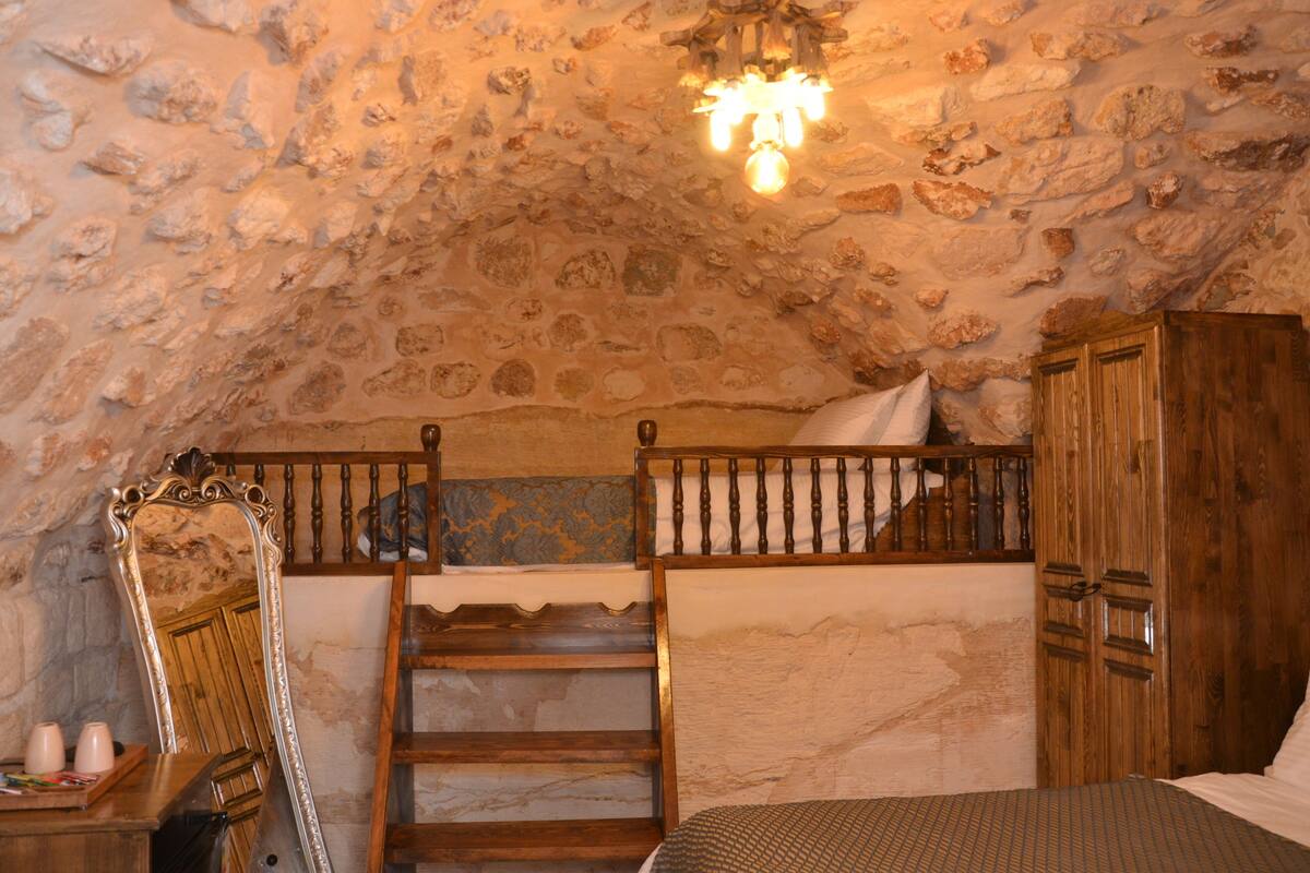 Una habitación rústica con techo de piedra, una litera de madera, un armario de madera y un espejo.