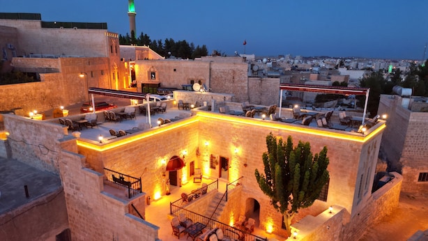 A rooftop terrace with stone walls, outdoor seating, and a view of the cityscape at dusk. - Mehmet Bey Konağı Butik Otel (Midyat)