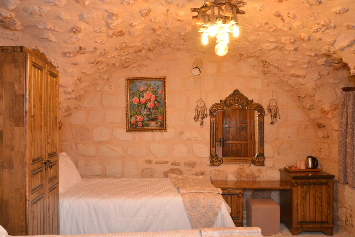 Un dormitorio con pared de piedra, un armario de madera, una cama con ropa de cama blanca, un escritorio de madera y un espejo.
