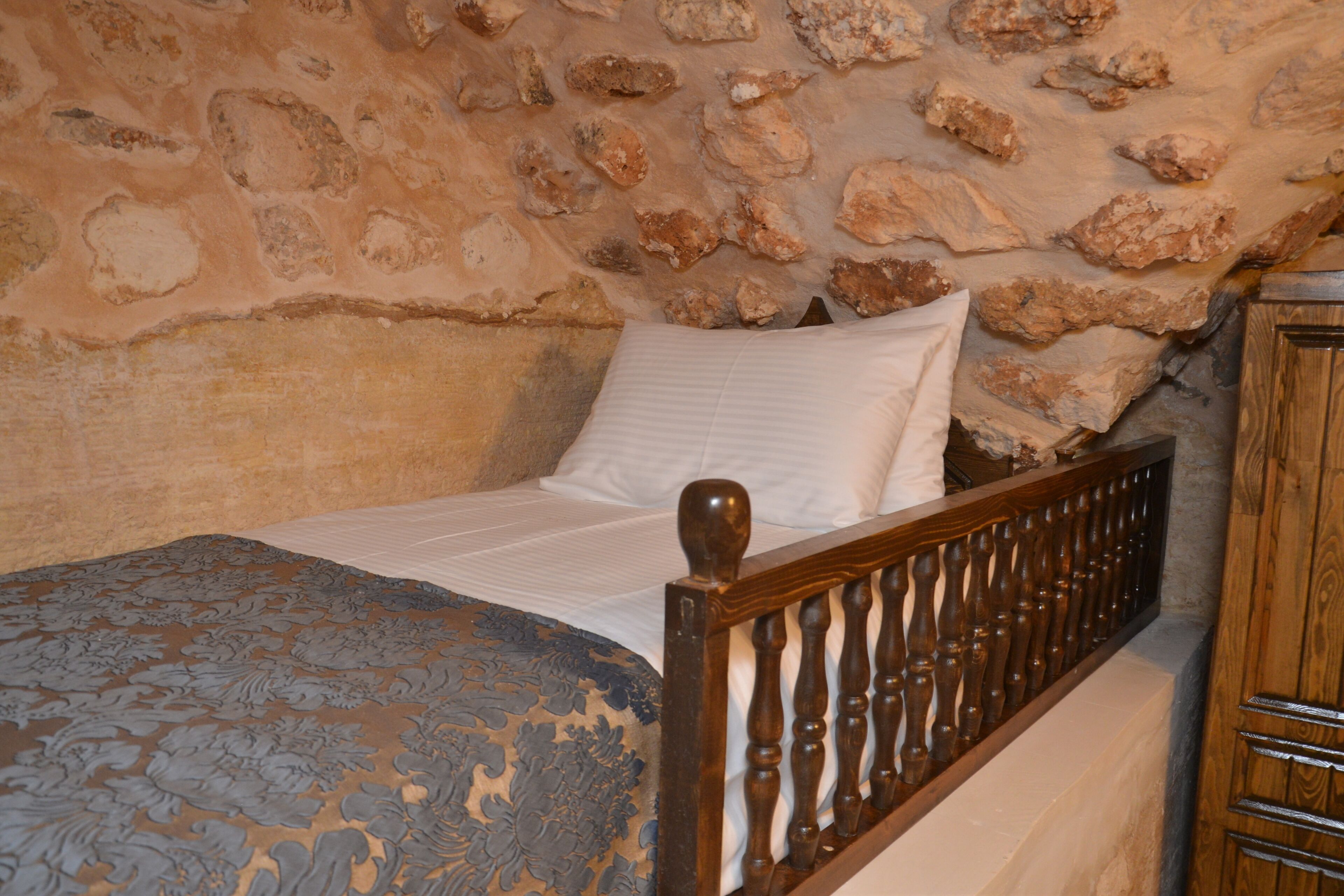 A bed with a wooden headboard, a stone wall behind it, and a wooden cabinet to the right.