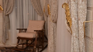 A room with a rocking chair, curtains, and a decorative wall piece. - Mehmet Bey Konağı Butik Otel (Midyat)