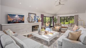 A spacious living room with a fireplace, comfortable seating, and large windows offering a view of greenery. - Calistoga Wine Ranch Estate (Calistoga)