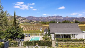 Un vignoble avec une piscine, un petit bâtiment et des montagnes en arrière-plan.