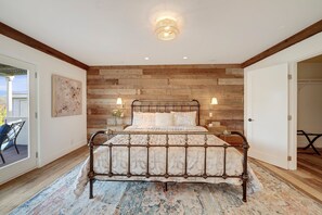 A bedroom with a wooden wall, a bed with a patterned bedspread, bedside lamps, and a ceiling light. - Villa in French Chateau Estate in Napa Valley (Calistoga)