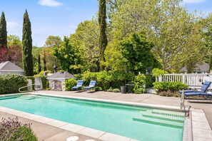 A rectangular swimming pool with a clear blue water surface, surrounded by a paved deck. There are two lounge chairs with blue cushions on the right side of the pool. - Villa in French Chateau Estate in Napa Valley (Calistoga)