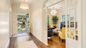 A hallway with wooden flooring, white walls, and a glass door leading to a living area with a sofa, yellow armchair, and a coffee table. - Casa Rosa in St Helena (St. Helena)