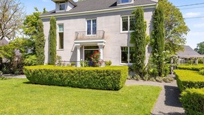 A two-story house with a balcony, a well-maintained lawn, and a garden with various plants and a hedge.