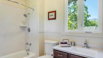 Un baño con bañera, inodoro, tocador y ventana con vista a árboles.
